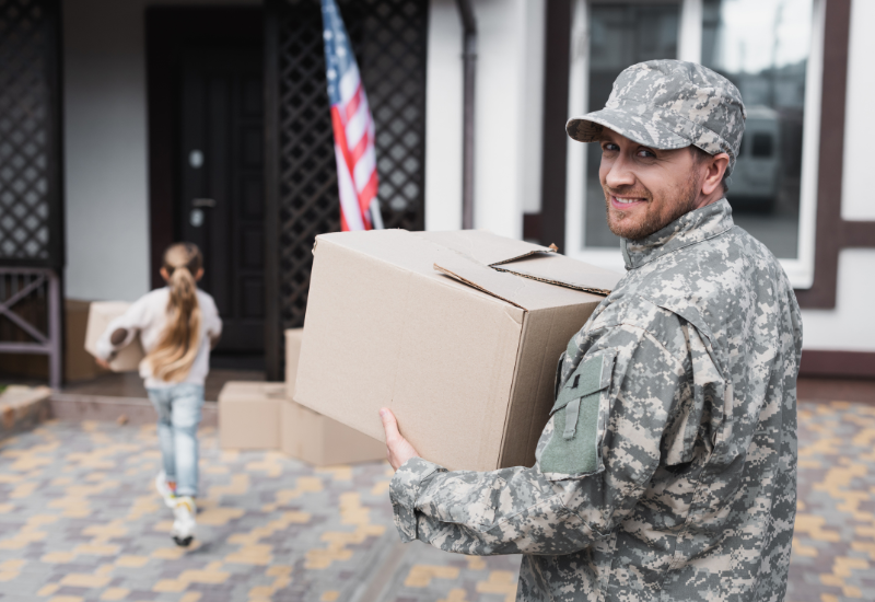 Man in military uniform carrying moving boxes into a home