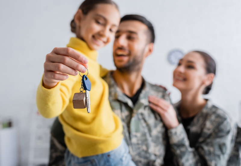 Man and woman in military uniform holding their daughter, looking at a house key