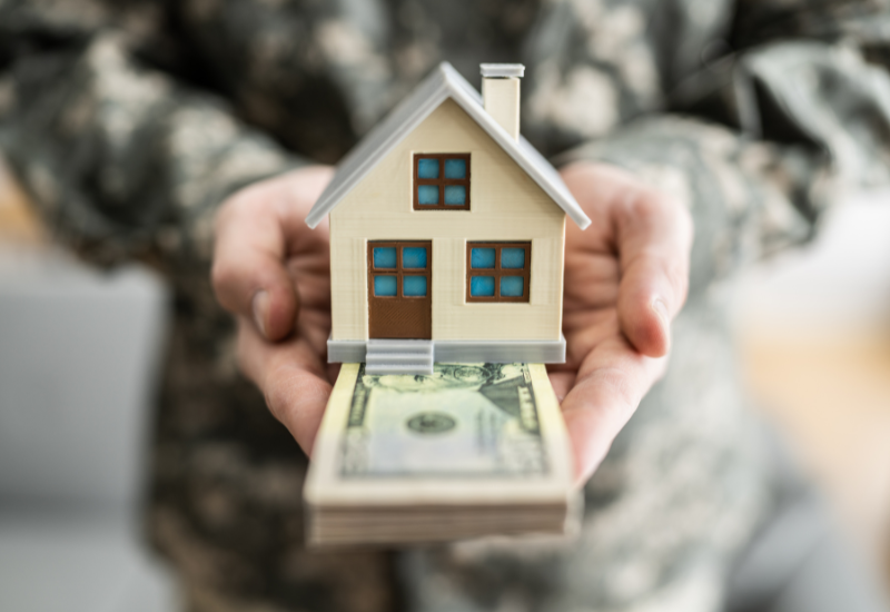 Man in military uniform holding a house figurine sitting on money